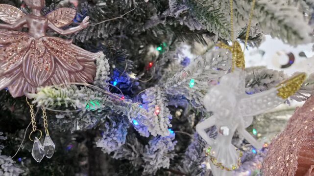 Pink glitter fairy ornament with crystal pendants hangs on a flocked tree with twinkling lights.