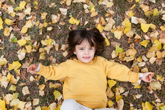 Smiling child lying in yellow autumn leaves, overhead view