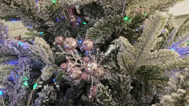 Pink glitter berry spray decorates a snowy flocked fir tree with softly glowing colorful lights.