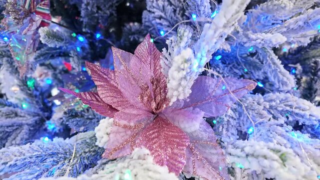 Pink glitter poinsettia decoration on a snowy flocked fir tree glowing with blue fairy lights.