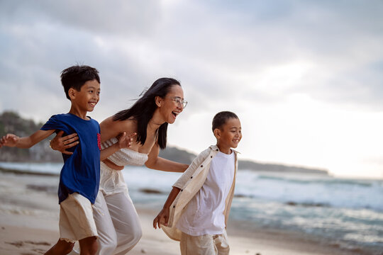 Happy asian mother talking and laughing with her young children on the beach