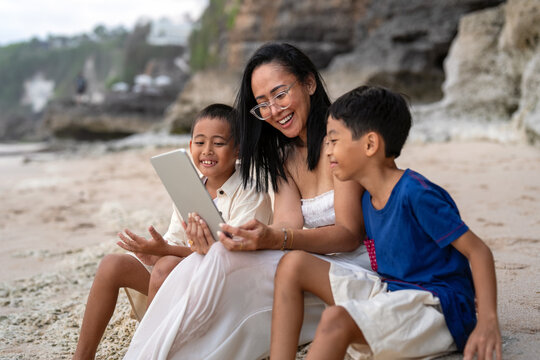 Happy asian family watching funny videos on a digital tablet together at the beach