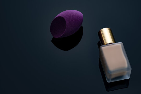 Purple makeup sponge on dark background. Soft makeup cosmetic sponge. Flat-ended makeup sponge with blur makeup foundation bottle. Liquid beige make-up foundation and beauty blender. Cosmetic product.