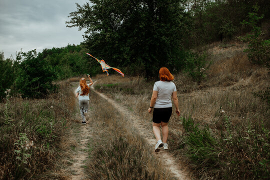 Mother and daughter running with kite on dirt road