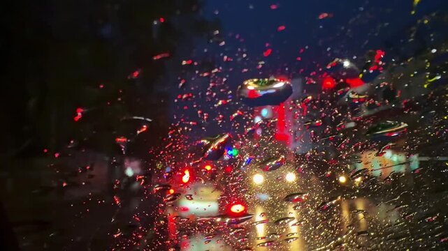 View from inside a moving car through a rain-soaked windscreen at night, with blurred streetlights and glowing light trails