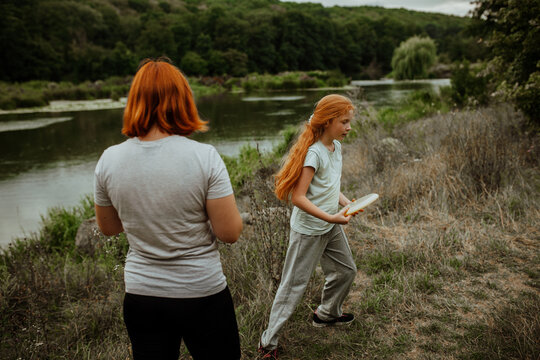 Mother and daughter playing frisbee near lake