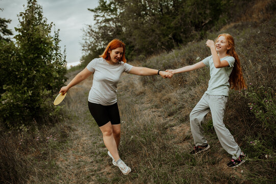 Playful mother and daughter tugging hands in meadow