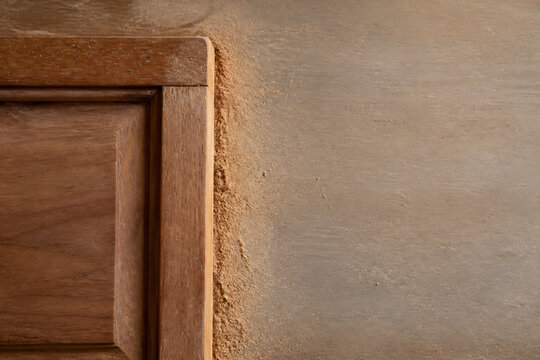 A close-up of a wooden door frame meeting a textured, unfinished wall surface.