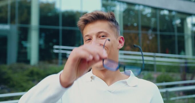 Close-up portrait of young Caucasian student man looking at camera on background of university outdoors. People concept