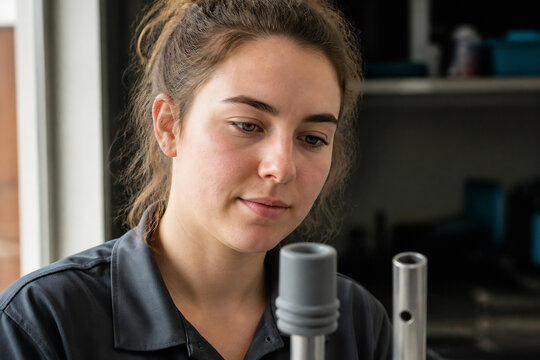 A young woman with brown hair is looking down at two metal objects in an indoor setting.