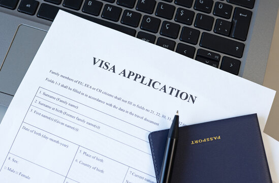 Filling form for immigration. Visa application form, pen, computer and passport on desk.