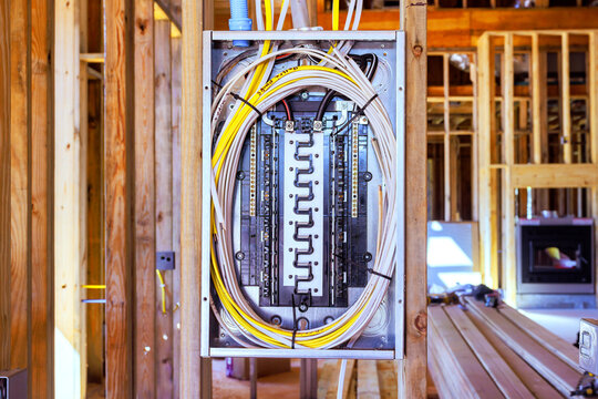 An electrical panel with bundled wires sits between exposed wood studs at building site under construction.