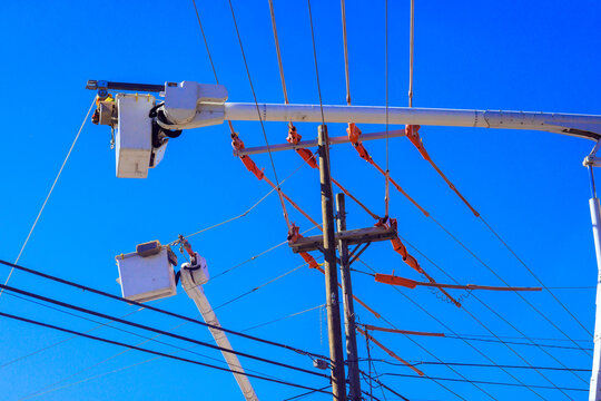 Bucket trucks reach power lines on utility pole during service, line works work in city.
