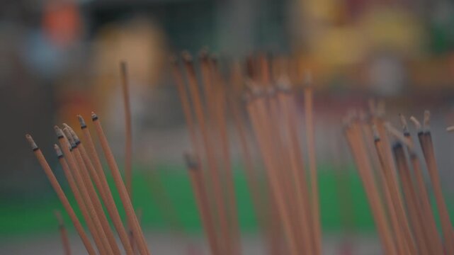 burning incense sticks releasing smoke, close up macro of spiritual offering at blurred buddhist temple 4k