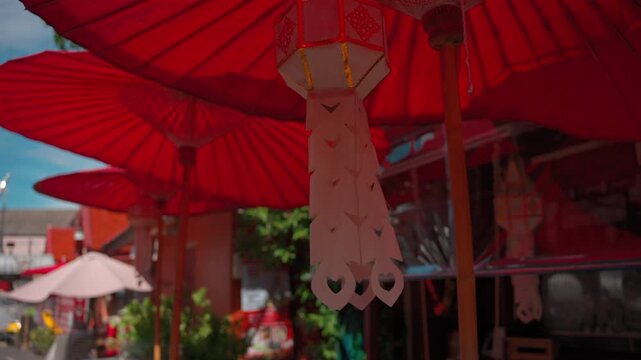 red paper umbrellas and white hanging lantern at thai temple, traditional lanna decoration outdoors during sunny festival 4k