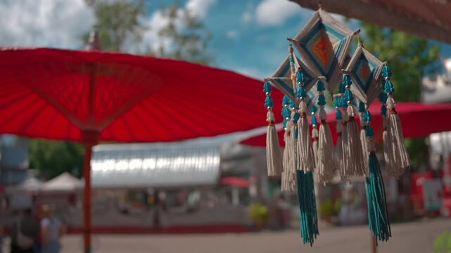 blue and white woven yarn ornament with hanging tassels, traditional thai lanna decoration near blurred red umbrella at sunny temple 4k