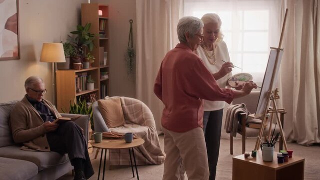 Diverse senior women painting artwork on canvas easel together in nursing home. Perfect for promoting active aging lifestyle, assisted living community, or art therapy programs