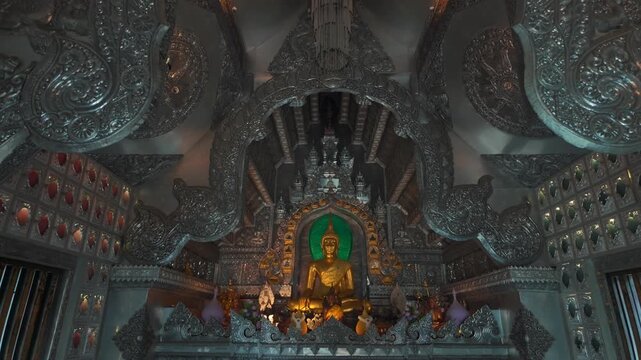 golden buddha statue inside ornate Silver Temple interior, sunlight illuminating intricate carved metal architecture of traditional Thai shrine Wat Sri Suphan 4k