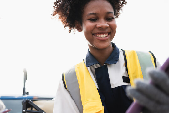 Smiling female field worker wearing a high visibility safety vest and gloves while using a smartphone beside a utility truck, representing mobile communication, outdoor work, and safety.