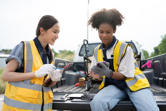 Two female environmental workers coordinate with a smartphone and clipboard beside a utility vehicle, representing field inspection, teamwork, communication, and site management.
