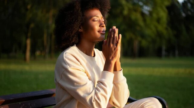 Woman meditating with folded palms in a green park, outdoor wellness retreat, holistic relaxation, mind body awareness