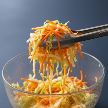 Lifting fresh coleslaw salad with metal tongs from glass bowl close up