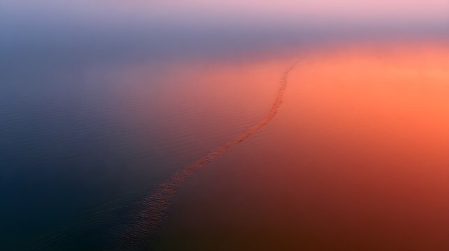 A single clear water trail cut through a misted orange sunset