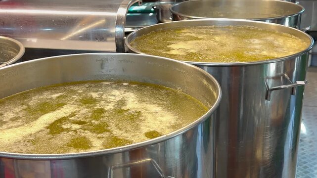 Hot broth boils inside large stainless steel pots at restaurant kitchen. Liquid food preparation, industrial cooking catering background and professional culinary production display.