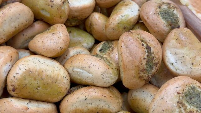 Fresh baked garlic and herb bread rolls inside bakery display. Golden mini buns with green seasoning, savory artisan snack selection, food retail assortment, culinary preparation product.