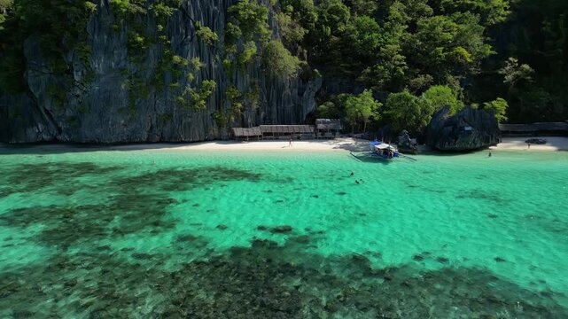 Aerial view of Coron Island beach featuring limestone cliffs, turquoise water, and a traditional outrigger boat on the white sand shore in Coron, Mimaropa, Philippines.
