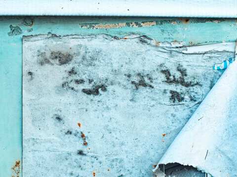 Torn peeling paper posters and cracked turquoise paint on a rusty metal wall, urban grunge texture with curling white paper remnants, abandoned weathered street surface