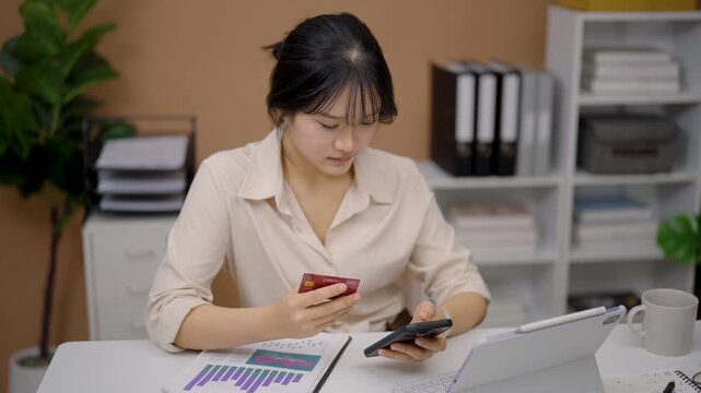 Young woman working at desk using smartphone and calculator with laptop and documents in organized office space