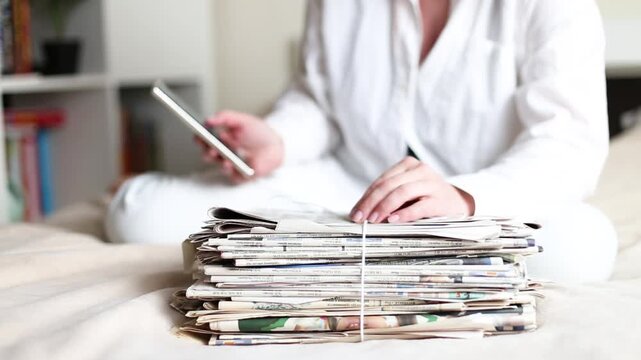 Person reading news on smartphone next to stack of old newspapers
