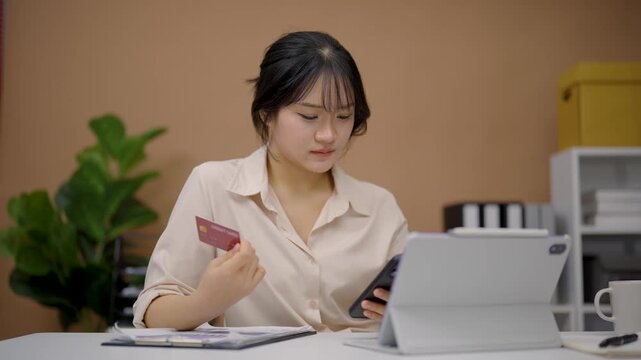 Young woman shopping online using smartphone and credit card with digital tablet and notebook on table indoors