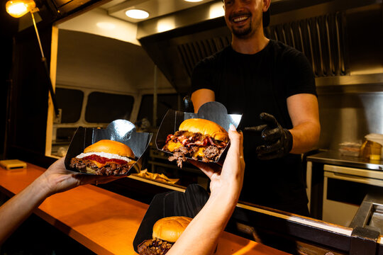 Customer receiving smash burgers from food truck vendor at night