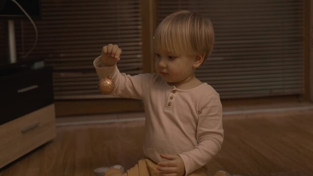 Warm holiday footage features a young boy who examines a small festive ornament with his mother nearby. This candid family scene illustrates sensory play, fine motor skills and togetherness.