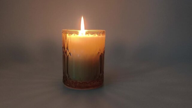 A burning scented candle in a decorative glass holder. The warm flame flickers gently, creating a cozy and tranquil atmosphere.