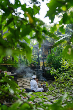 Man Sits in Garden and Prays While Smoke Rises in Bali