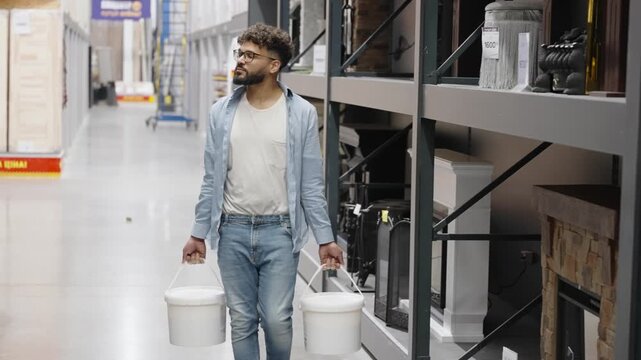 Focused man walking with paint buckets in hardware store