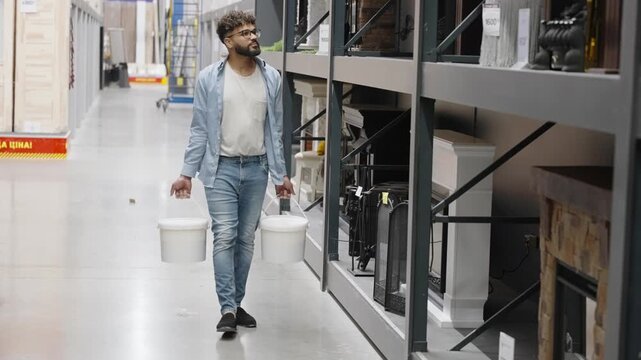 Focused young man carrying paint buckets in a hardware store