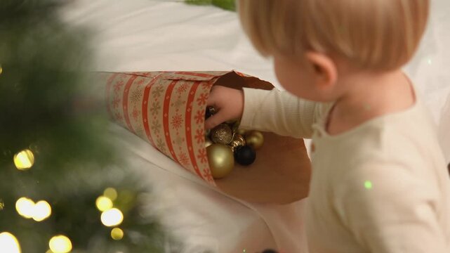 Warm holiday footage features a young boy who studies a shiny ornament with focused toddler attention. This candid family scene illustrates concentration, sensory discovery and togetherness.
