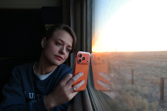 Woman taking selfie with smartphone on train at sunset