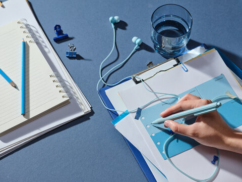 Hand writing in planner with blue stationery and headphones on desk