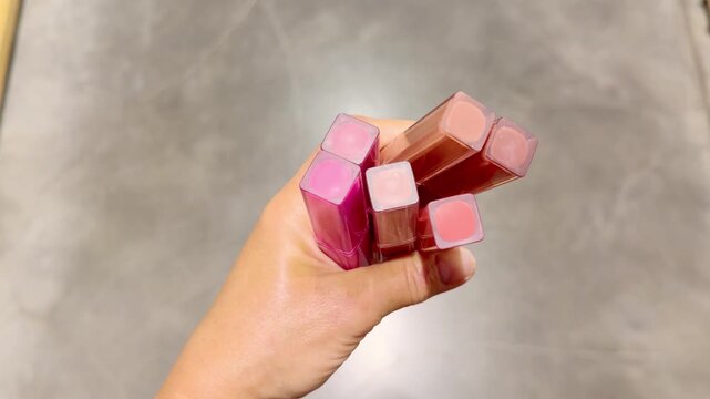 Hand Holding Several Colorful Lipsticks in Cosmetics Store &ndash; Choosing Between Different Shades Against Makeup Shelves