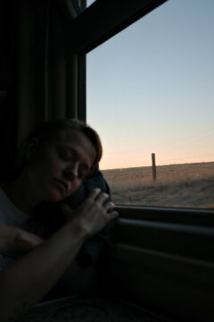 Woman sleeping on train leaning against window at sunset