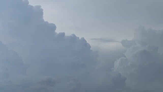 Large cumulus clouds moving and changing shape across a pale blue sky, with soft sunlight filtering through the clouds, capturing atmospheric weather and nature, Timelapse footage