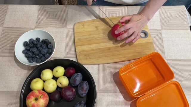 Fruit slicing preparation, Chopping nectarines with arranged blueberries and apples on wooden surface, Carefully cutting nectarines on wooden board with blueberries and apples positioned nearby