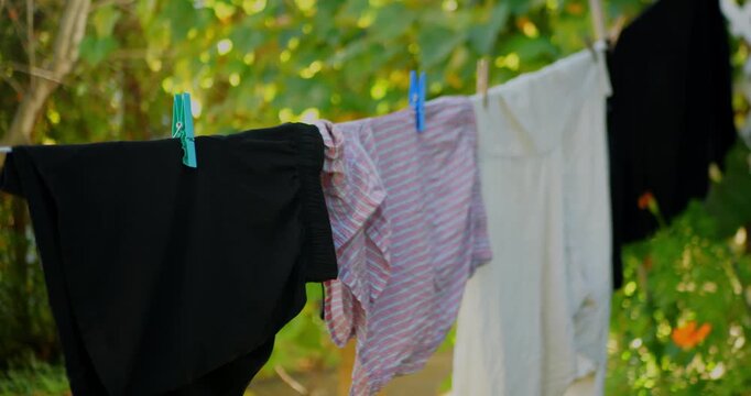 Close-up of clothes drying on a clothesline in a sunny garden. Fresh laundry, household chores, eco living, and outdoor air drying.