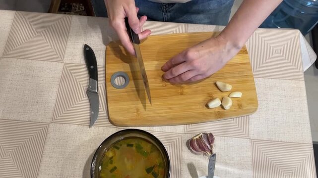 Cooking garlic preparation, Chef mincing garlic nearby soup, Chef skillfully minces garlic beside bowl of soup, Rustic kitchen scene with chef slicing garlic beside bowl of soup on countertop