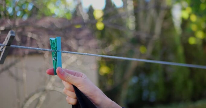 Close-up of a hand releasing a blue clothespin from a clothesline in a garden. Outdoor laundry, domestic chores, air drying, and sustainable living.